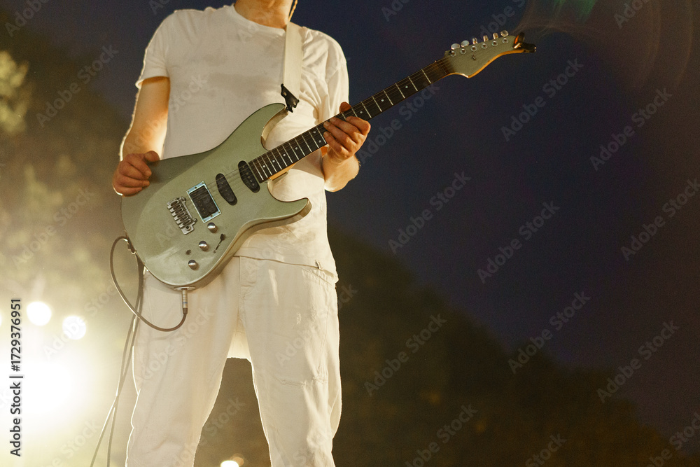 Obraz premium Musician performing on stage with electric guitar during a nighttime concert in an outdoor venue