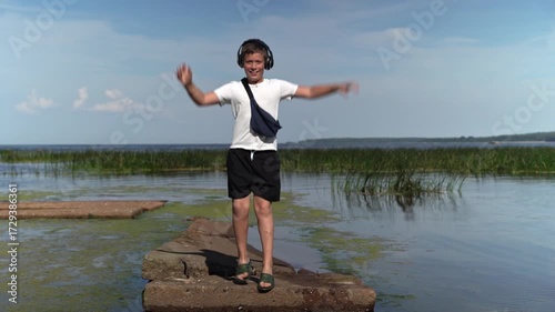 Happy energetic boy dancing on pier wearing headphones