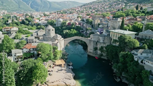 Mostar, Bosnia and Herzegovina Aerial dolly drone video flying along the Neretva River, bypassing the Old Bridge, and centering on Koski Mehmed Pasha Mosque with surrounding old town and hills