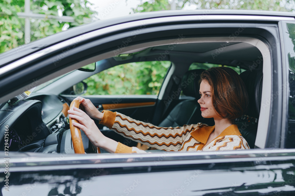 Naklejka premium A woman driver sits in a modern car with hands on the steering wheel, focused on the road as daylight filters through the window.