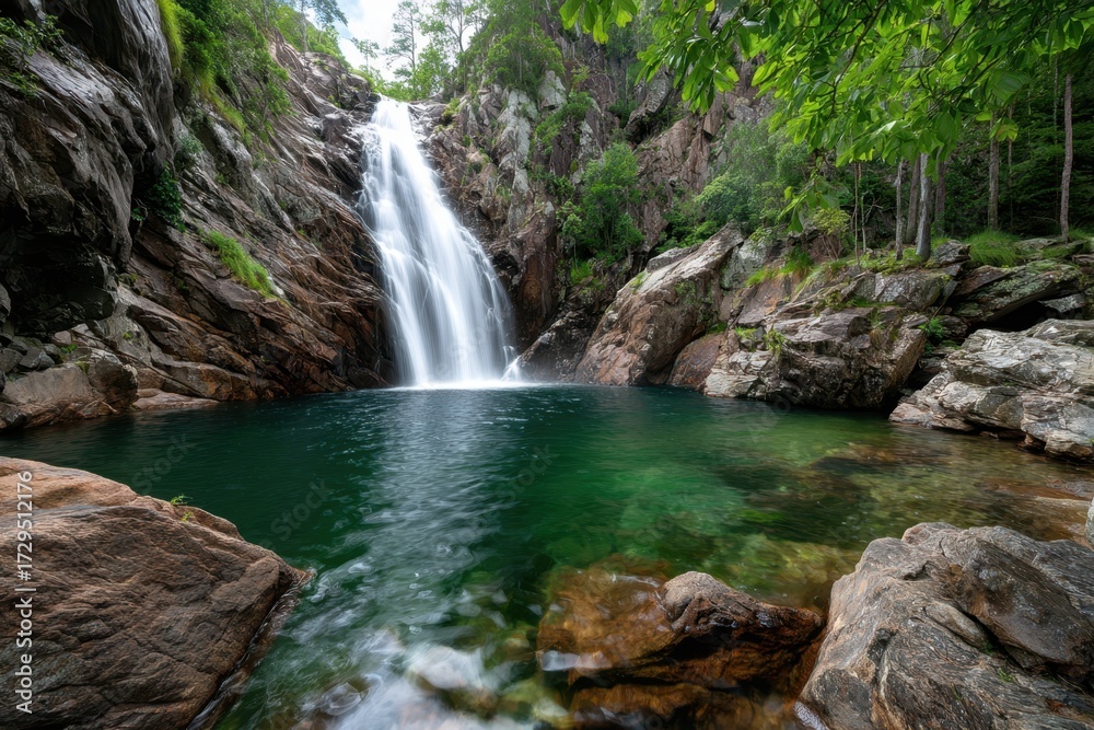 Fototapeta premium Waterfall cascades into a clear green pool in a rocky gorge