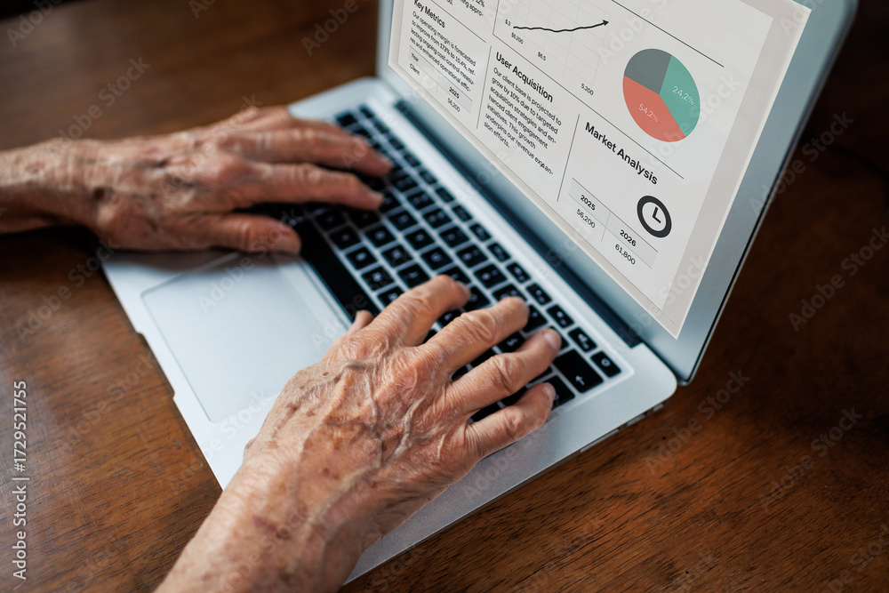 Fototapeta premium elderly person's hands typing on laptop while reviewing business reports