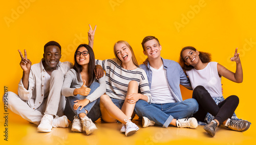 Quadro em tela Multiracial carefree teenagers sitting on floor, embracing and having fun over y
