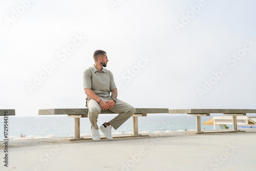 Photography A man is sitting on a bench by the ocean