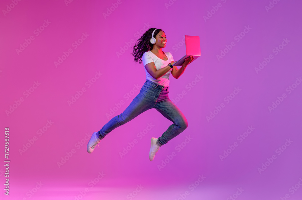 © Prostock-studio - Happy Black Woman In Wireless Headphones Jumping With Laptop In Neon Light, Cheerful Young African American Lady Working Online Or Playing Video Games On Computer, Enjoying Modern Technologies © Prostock-studio - Happy Black Woman In Wireless Headphones Jumping With Laptop In Neon Light, Cheerful Young African American Lady Working Online Or Playing Video Games On Computer, Enjoying Modern Technologies