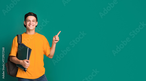 Teen student with books pointing on copy space against turquoise background