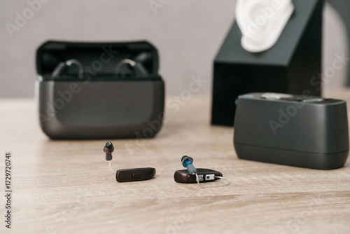 Modern digital hearing aids with charging case on wooden table in audiology clinic. Hearing aid, charger, and ear model for fitting and demonstration.