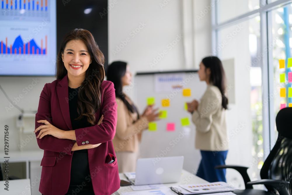 Fototapeta premium Smiling young Asian businesswoman crossing arms in office