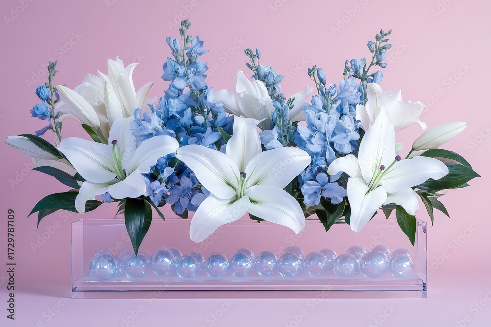 Obraz premium A delicate arrangement of white lilies and light blue delphiniums sits gracefully in a clear acrylic box, creating a serene and elegant display.