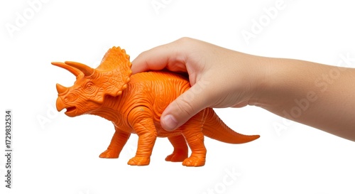 A childs hand holds an orange plastic Triceratops toy against a white background
