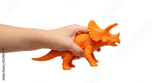 A hand holds an orange plastic triceratops toy against a white background