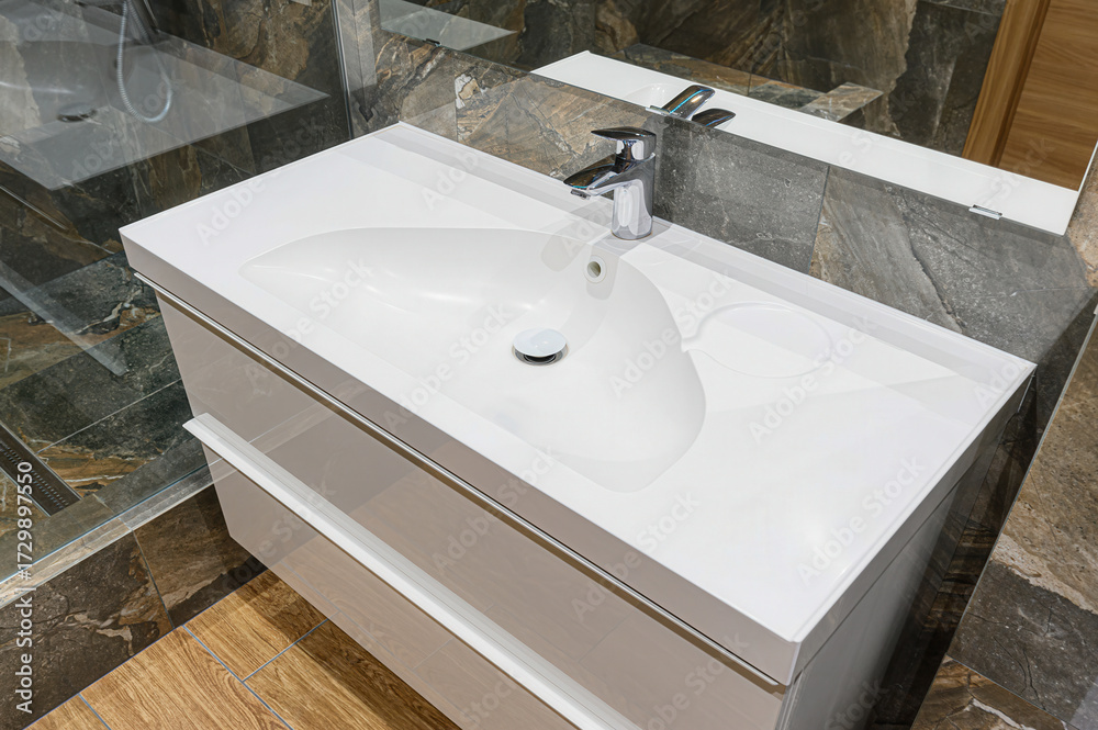 Fototapeta premium A modern bathroom vanity with a white sink, chrome faucet, and drawers. Marble and wood textures accent the space