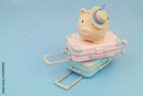 Pink and blue travel suitcases with beach hat and piggy bank on blue background. Copy space for text. Travel budget concept.