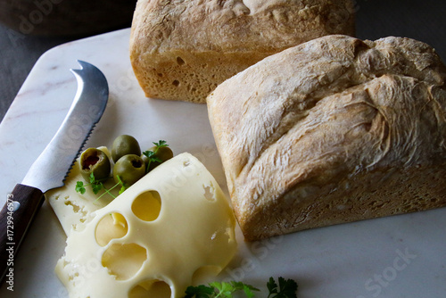 Two loaves of spelt bread and swiss cheese with a knife and olives.