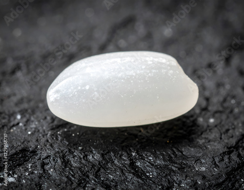 An extreme close-up of a single grain of white rice on a black, textured surface. A simple, minimalist macro for food and ingredient concepts. Generative AI
