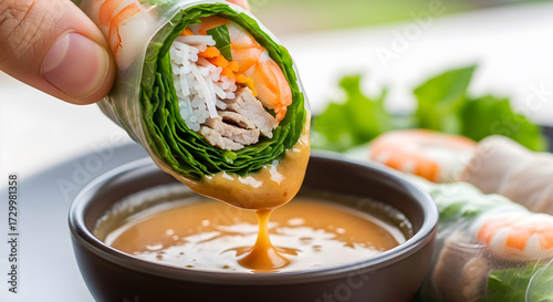 Fresh spring roll being dipped into peanut sauce closeup.