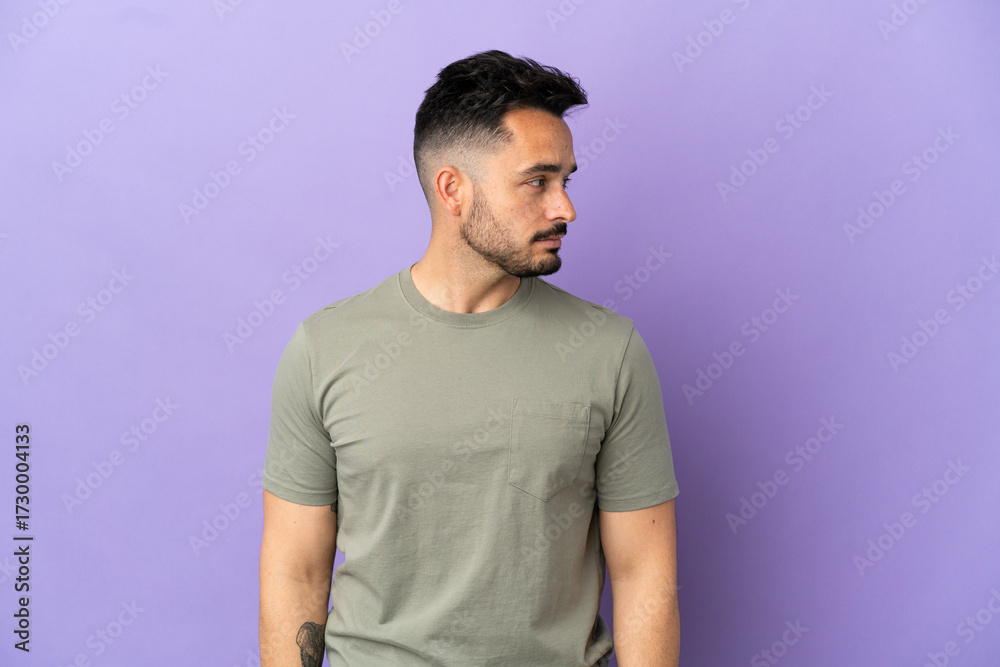 Obraz premium Young caucasian man isolated on purple background looking to the side