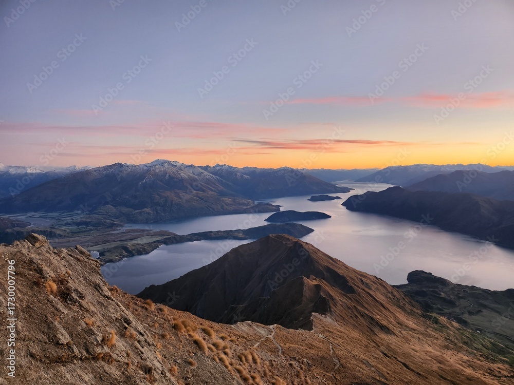 Fototapeta premium Sunrise over Roy’s Peak in Wanaka, New Zealand, seen from the hiking trail. Golden morning light illuminates the mountains and Lake Wanaka, creating a breathtaking landscape for travel and adventure l