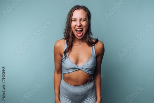 Woman in blue activewear expressing excitement against blue background.