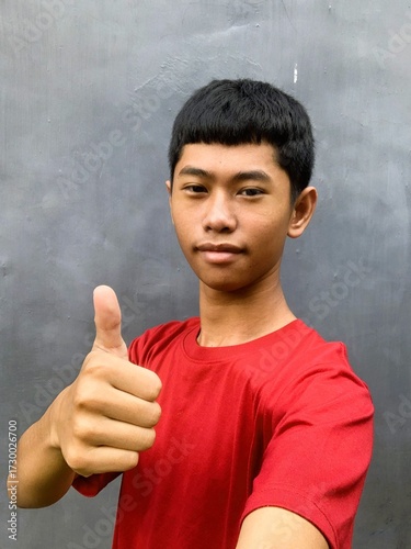 A southeast asian teenager with an expressive face poses for a selfie taken with their own hand