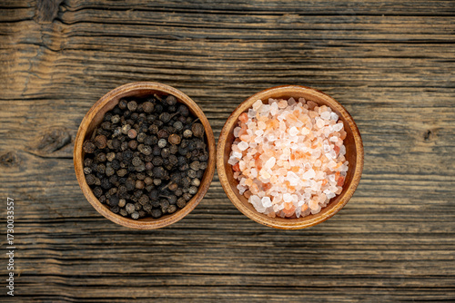 Two wooden bowls with pink salt and black peppercorns