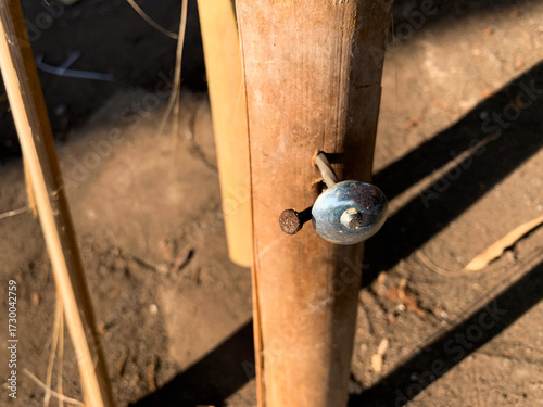 Bright sunlight highlights the surface of bamboo and the reflective metal head of the nail. Focus is on the connection point, emphasizing manual labor, building, and natural wood material