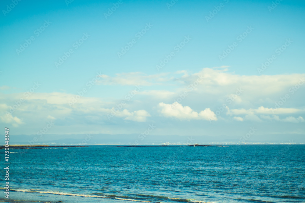 Obraz premium Blue ocean waves under cloudy sky with distant coastline