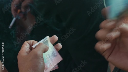 Close-up of workers’ hands holding and counting Indonesian rupiah banknotes, shifting the money between fingers.