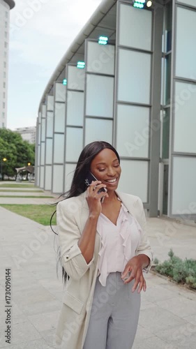 Vertical slow motion video of Elegant African american businesswoman walking and talking on phone outside office building