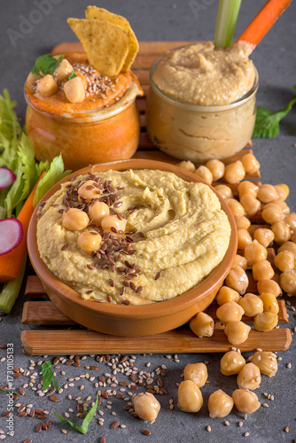 Assorted hummus bowls with chickpeas, flax seeds and fresh vegetables. Healthy homemade dip ideal for snacks and Mediterranean cuisine