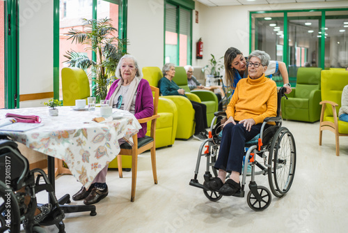 Tableau sur toile Senior women sitting in wheelchair and at table, a young caregiver assisting in