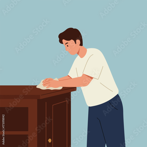 Young man cleaning a wood cabinet with a cloth in a simple interior scene