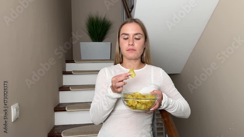Crispy potato chips. A teenage girl standing on the stairs relaxing while enjoying a bowl of crispy potato chips.