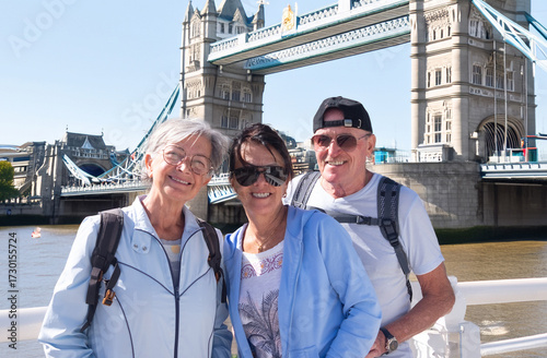 A happy group of elderly people in their seventies visiting London posing for a souvenir photo at London Bridge, enjoying their travel destination and the sunny day