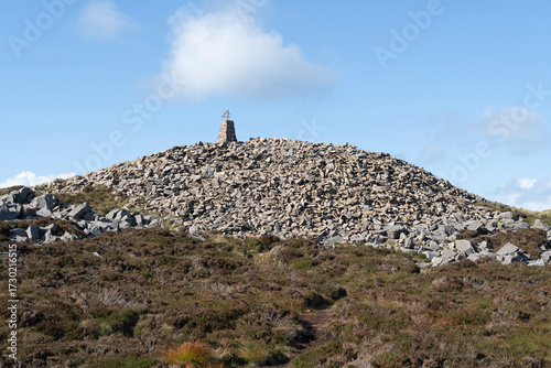 Path leading to the summit trig point on Yr Eifl mountain, Gwynedd, Wales, UK against a blue sky with cloud.