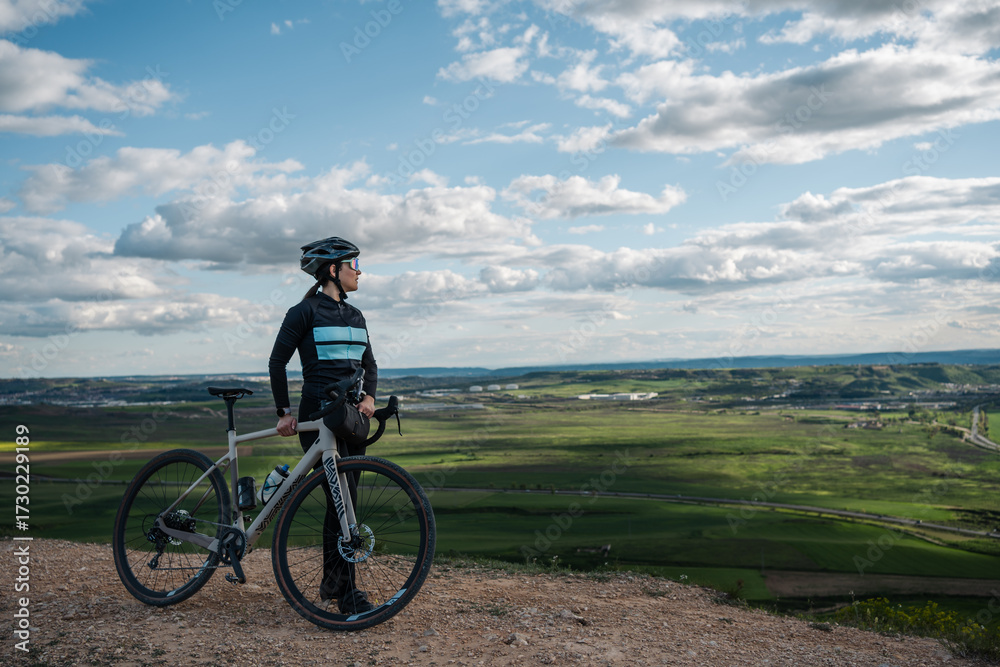 Obraz premium Young woman cyclist enjoying scenic view from hilltop with gravel bike