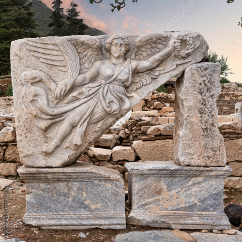 Ancient marble relief of winged Nike holding a wreath, Ephesus, Selcuk, Turkey. Historic archaeological ruins with green hills and sky