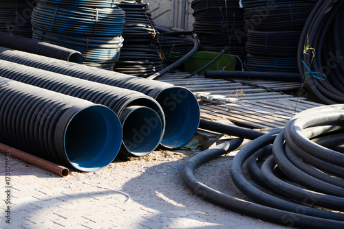 Stack of Corrugated Drainage Pipes and Coiled Utility Cables