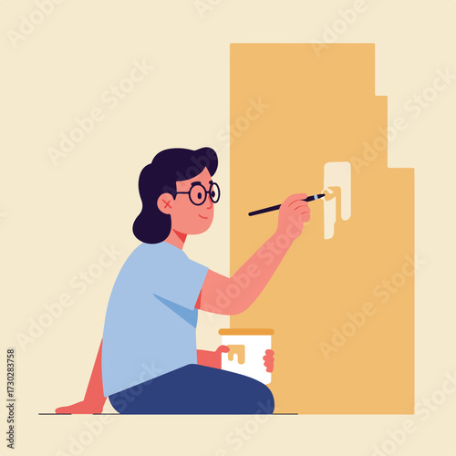 Artist painting a wall with a brush, sitting on the floor with a paint container