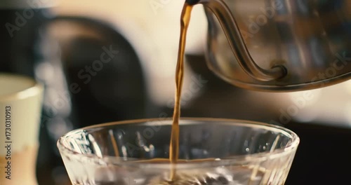 Coffee being poured into a clear glass cup indoors