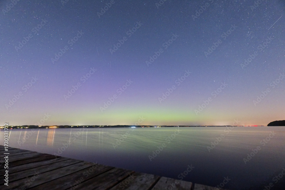 Naklejka premium Aurora over sea with wooden pier in Solituede in Flensburg and bright starry sky.