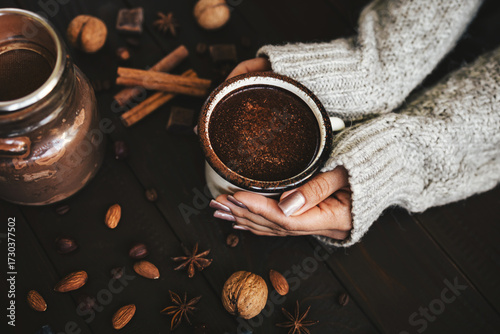 Female hands in sweater holding mug of hot chocolate drink on rustic wooden background, cozy seasonal scene