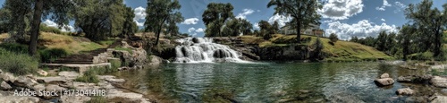 Panoramic view of a tranquil waterfall cascading into a pool, surrounded by lush greenery and trees