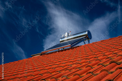 Solar water heater boiler on rooftop , dark blue sky with white washed clouds.