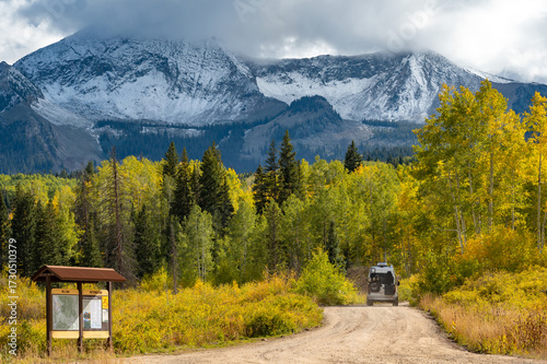 Camper van on dirt road with beautiful fall foliage scenery of snowcapped Rocky mountain, yellow aspen and pine trees in Gunnison National Forest near Crested Butte, Colorado, USA.