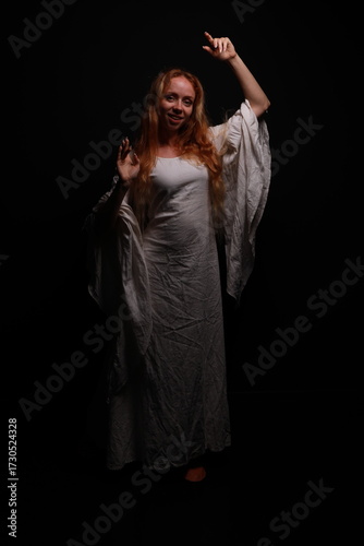 Full length portrait of a young red-haired woman in a vintage white dress in a low key