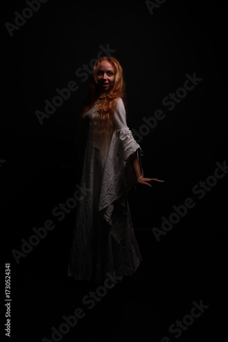 Full length portrait of a young red-haired woman in a vintage white dress in a low key