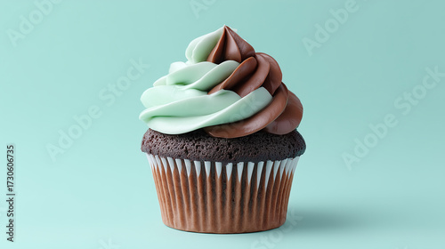 Chocolate cupcake with swirl frosting in mint green and chocolate brown colors sits against soft teal background, creating delightful and appetizing treat