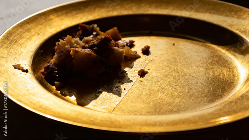 A partially eaten meal on a golden plate with remnants of food and crumbs under warm lighting