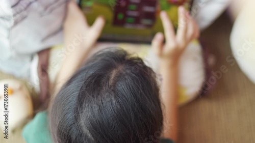 Top-view of an Asian kid, a young girl, intensely playing game on her mobile phone or tablet. This shows her hands interacting with the screen, modern childhood moment of digital entertainment.